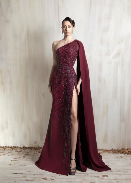 Burgundy one-shoulder gown with beaded detailing and dramatic cape