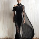 Black asymmetrical gown with sheer embellished sleeve and flowing cape.