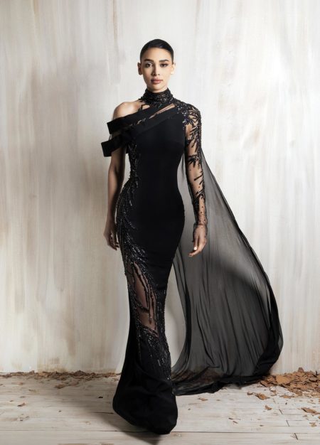 Black asymmetrical gown with sheer embellished sleeve and flowing cape.
