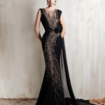 Black gown with golden cascade embroidery and sleek cape detail.