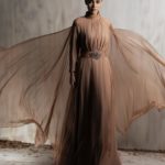 Flowing mocha chiffon gown with ethereal cape sleeves.